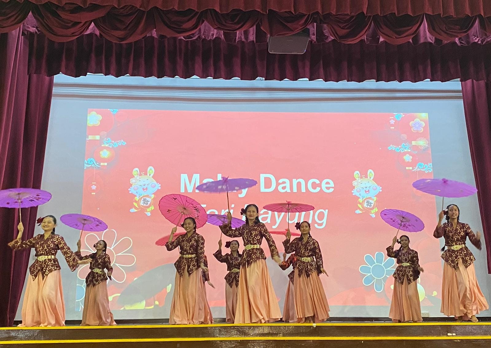 Girls in batik costumes perform Malay Dance Tari Payung on stage, holding colorful parasols.